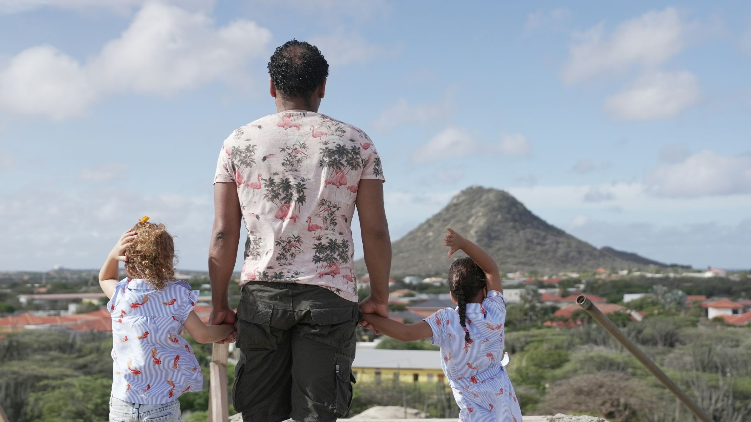 Pai de mãos dadas com as duas filhas olhando a paisagem