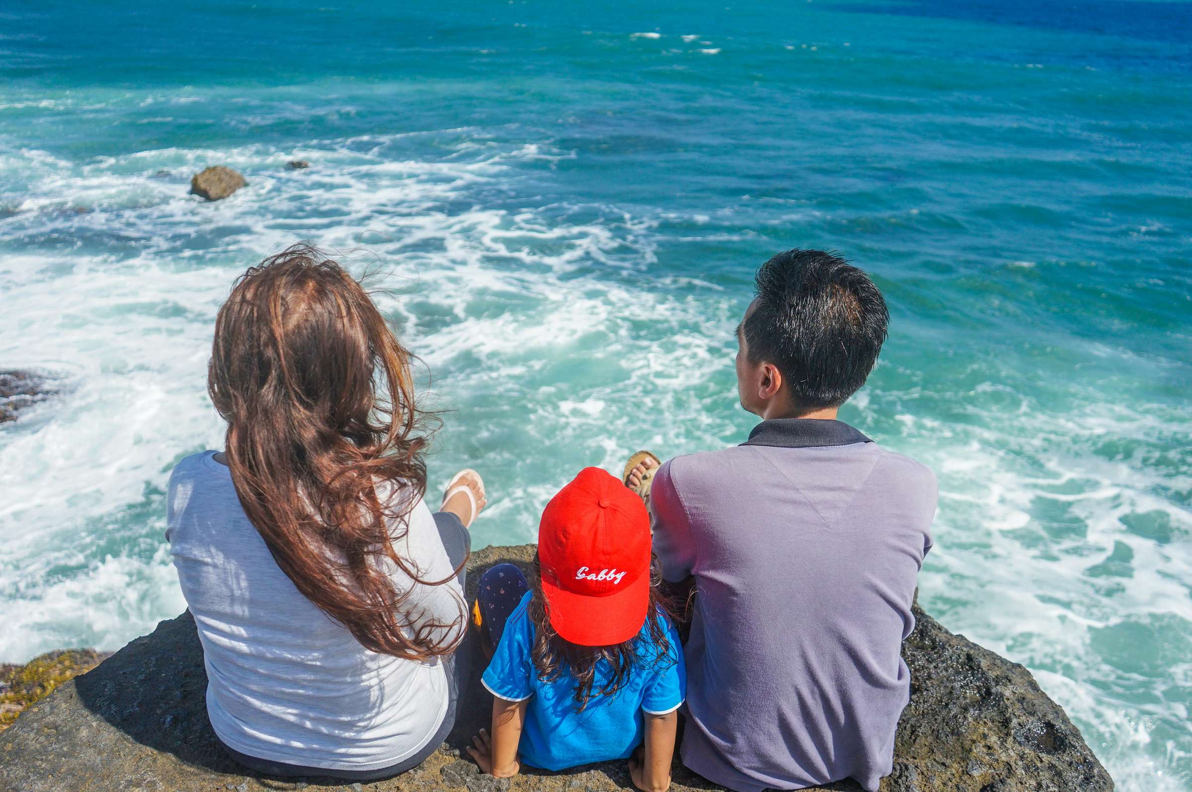Família sentada numa pedra olhando o mar
