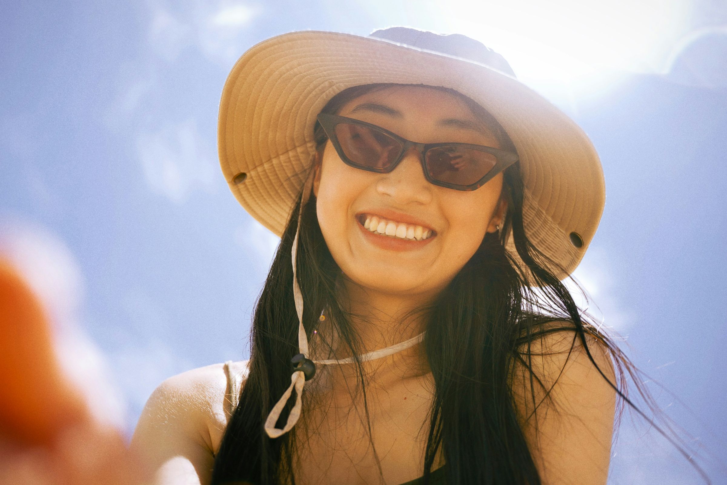 Mulher de chapéu e óculos escuros sorrindo ao sol
